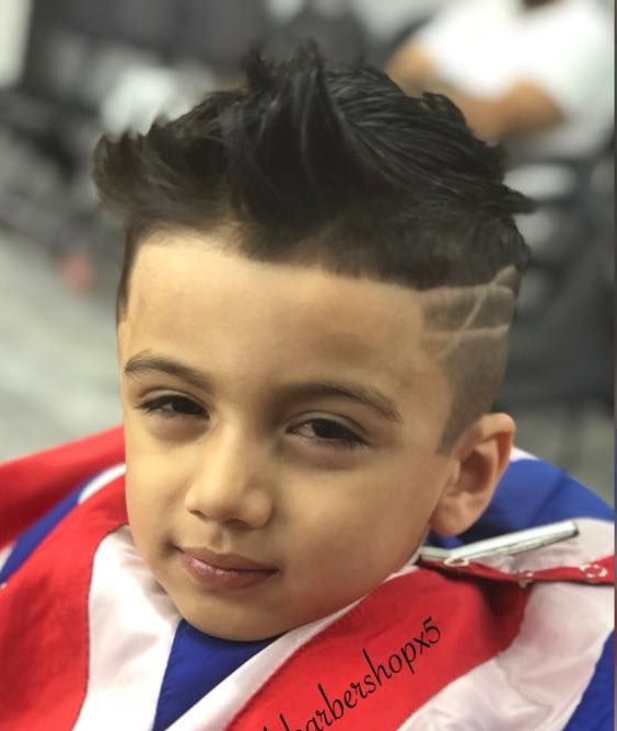 Child with spiked haircut and shaved line design, wearing a red, white, and blue sports jersey.