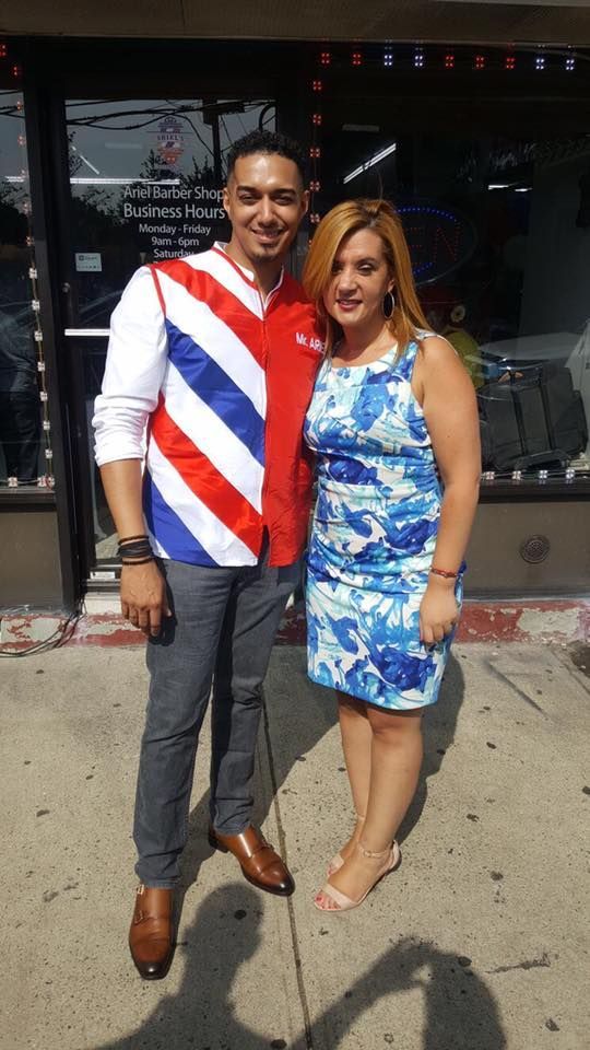 Two people standing together on a sidewalk, smiling in front of a storefront.