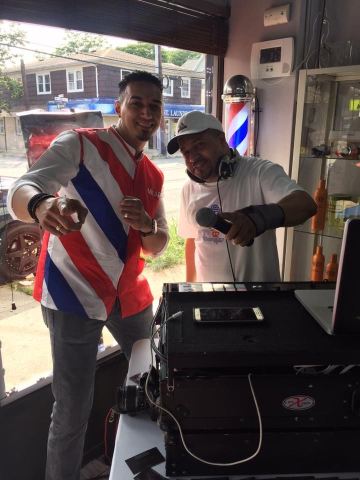 Two men posing behind a DJ booth, one pointing at the camera in a bar-like setting.