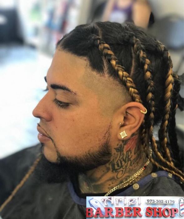Side profile of a man with braided hair and a fade haircut, wearing earrings in a barbershop.