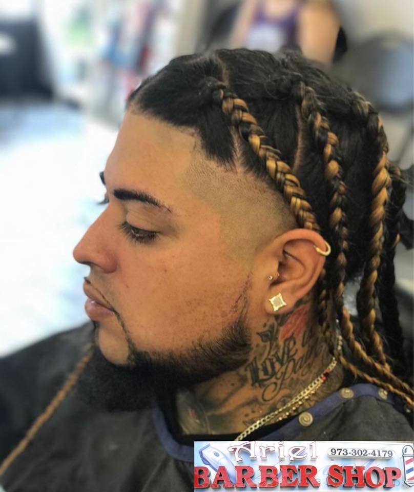 Profile of a person with braided hair, shaved sides, and a neck tattoo in a barber chair