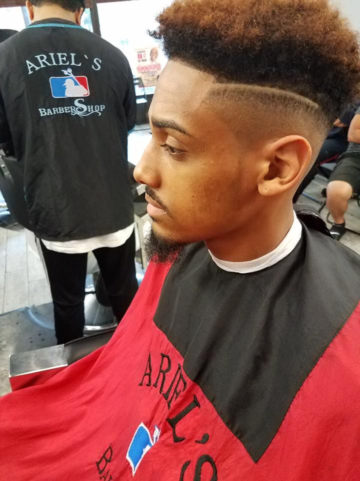 Man getting a fresh fade haircut in a barber chair, wearing a red and black cape.