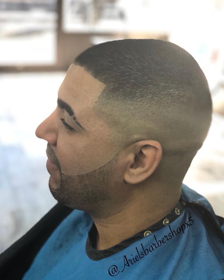 Side profile of a man with a close-cropped fade haircut and trimmed beard in a barber chair.