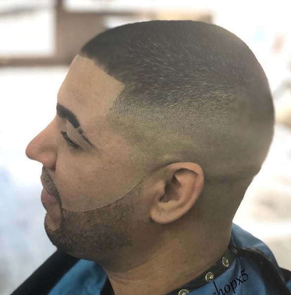 Profile of a man with a close fade haircut and lined beard in a barber chair