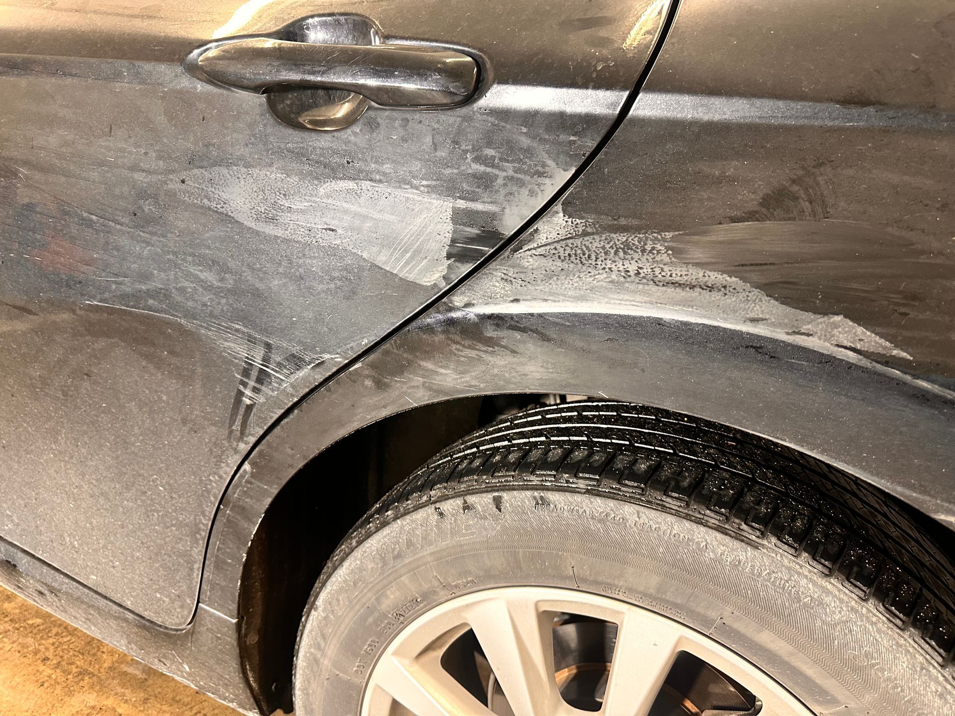 Dark car with damage along the rear door and wheel well, covered in white residue.