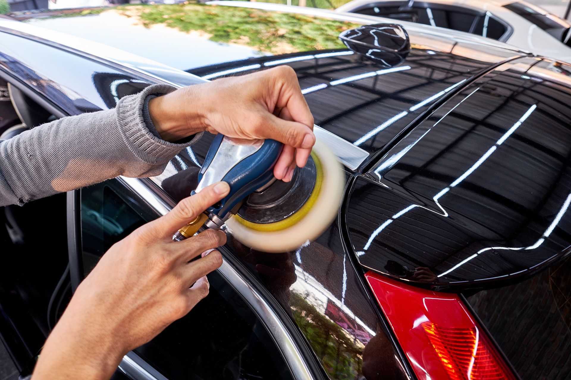 Person polishing a black car with a buffer; close-up of hands and car's surface.