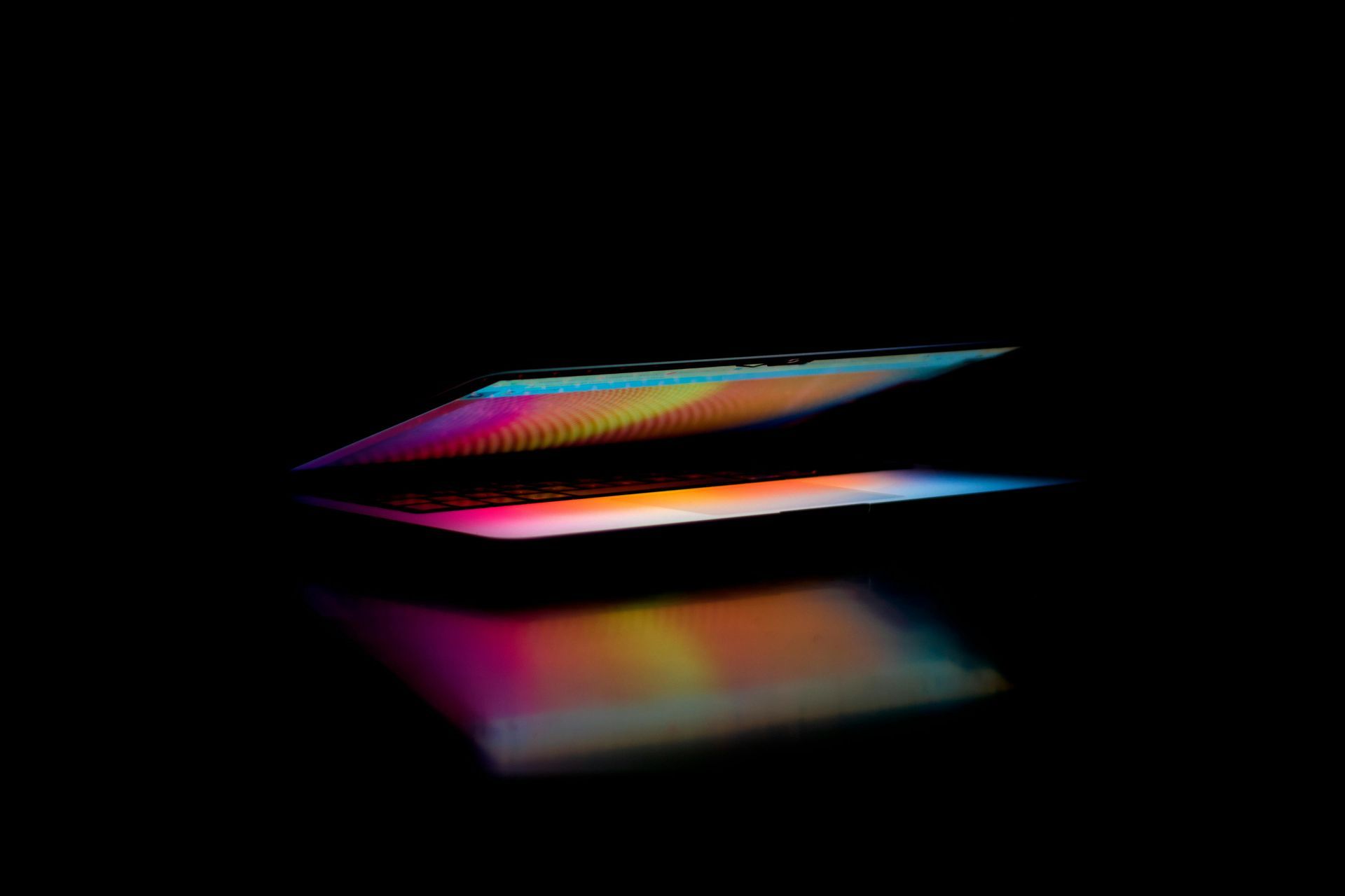 A laptop with a rainbow colored screen is sitting on a table in the dark.