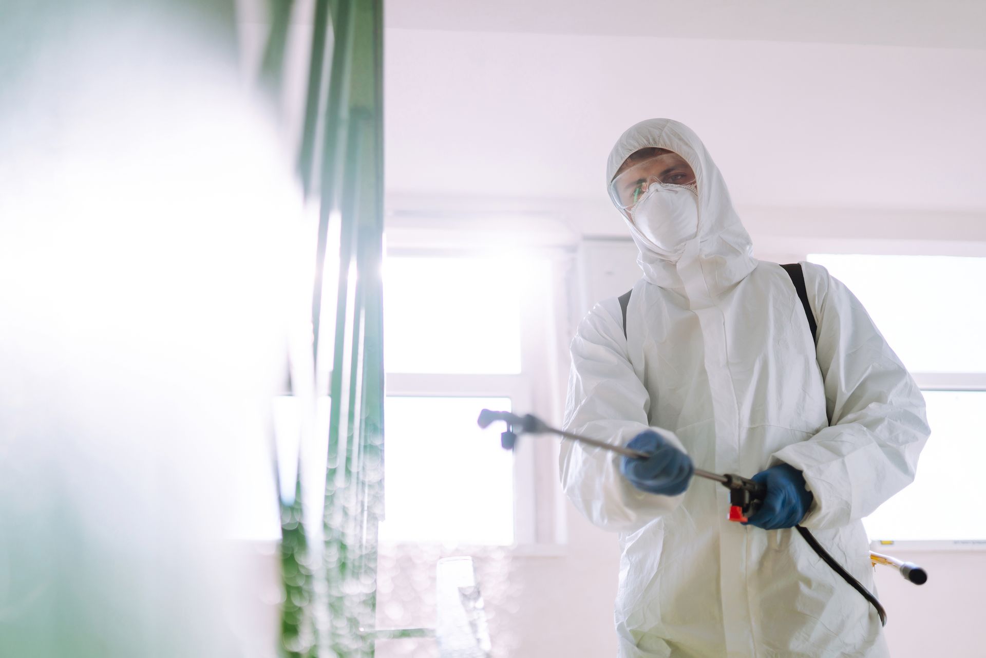 A man in a protective suit is spraying a room with a sprayer.