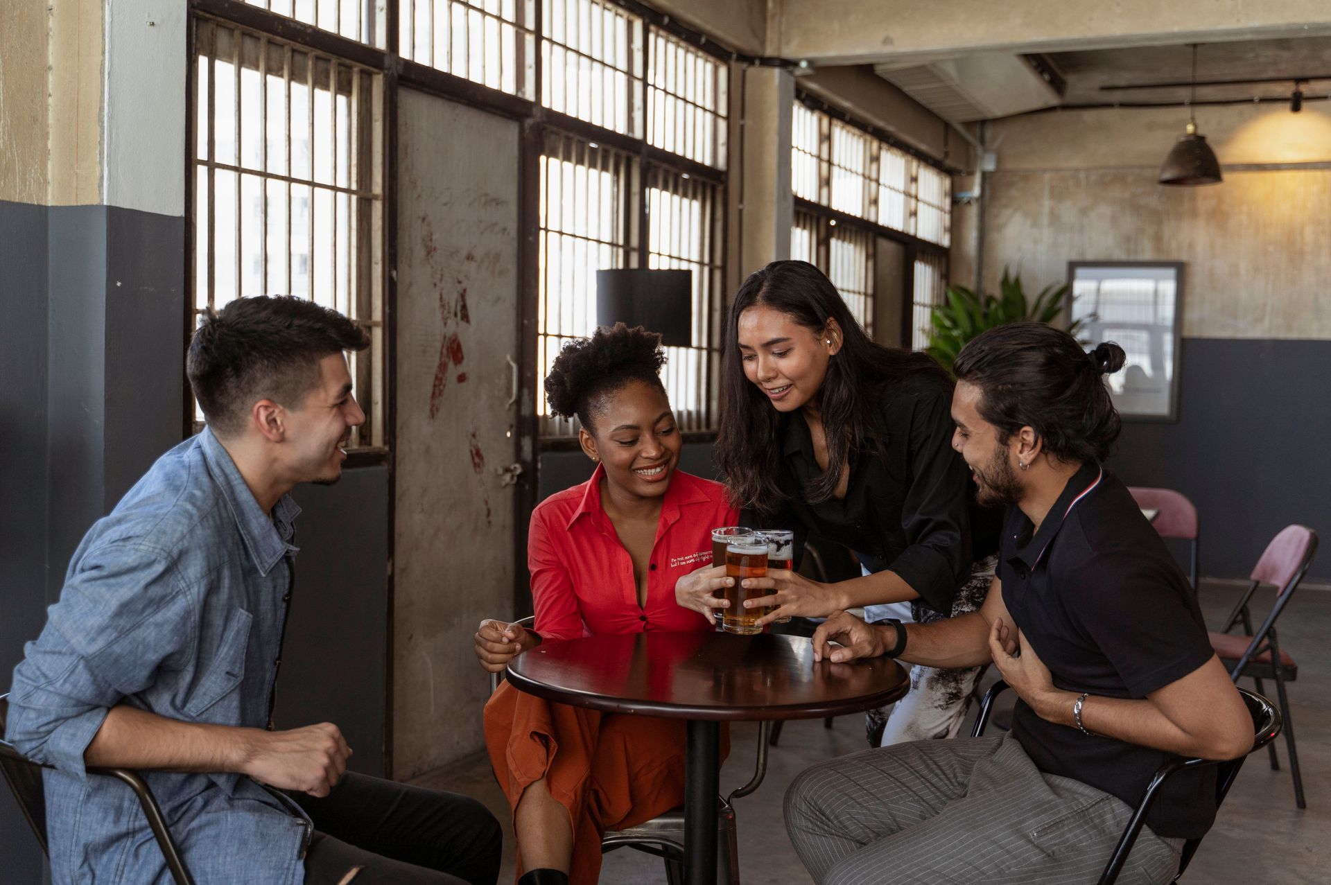 Four coworkers gathered around a table in a casual office, looking at a phone and talking.