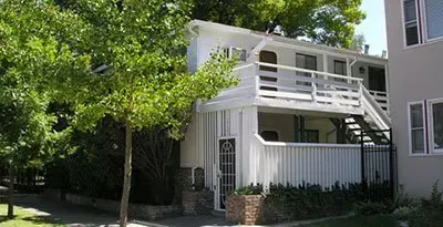 A white house with a balcony and stairs is surrounded by trees.