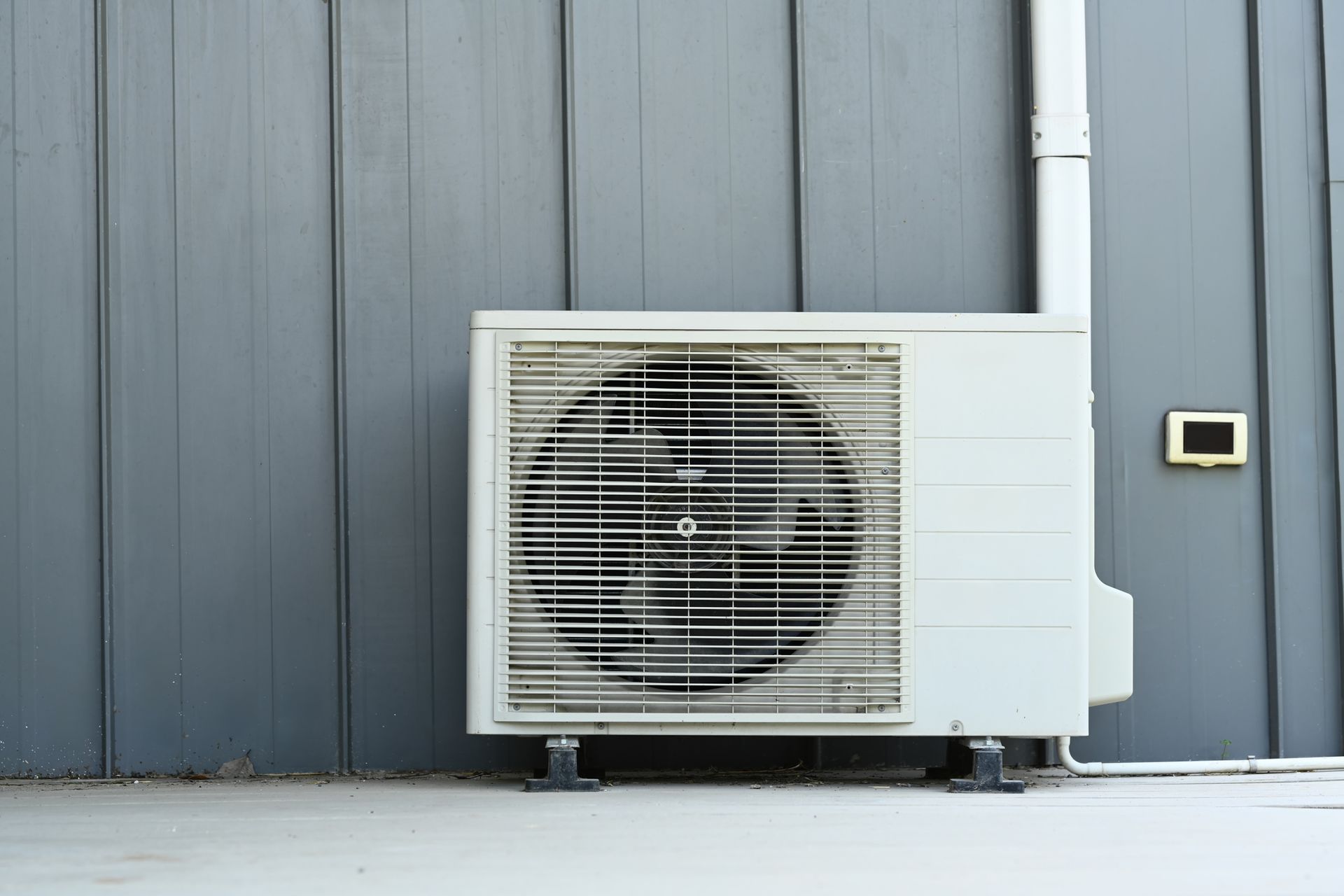 A white air conditioner is mounted to the side of a building.
