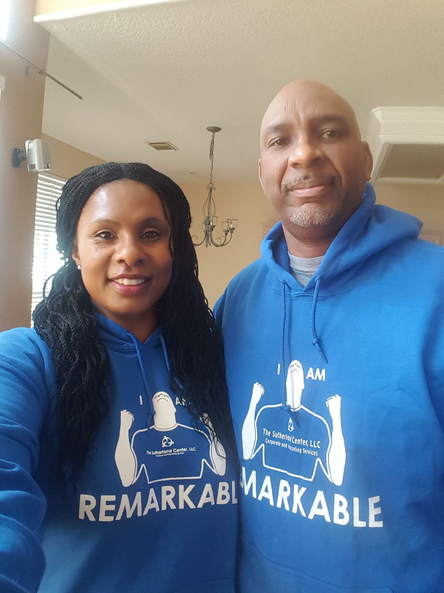 Two people in blue hoodies standing indoors, smiling at the camera.