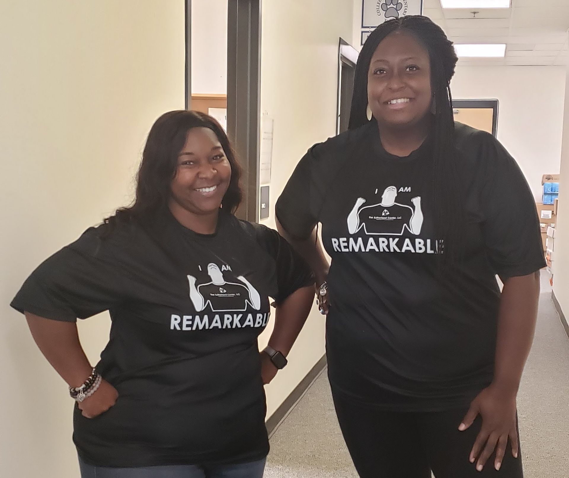 Two women in black “Remarkable” T-shirts posing indoors and smiling