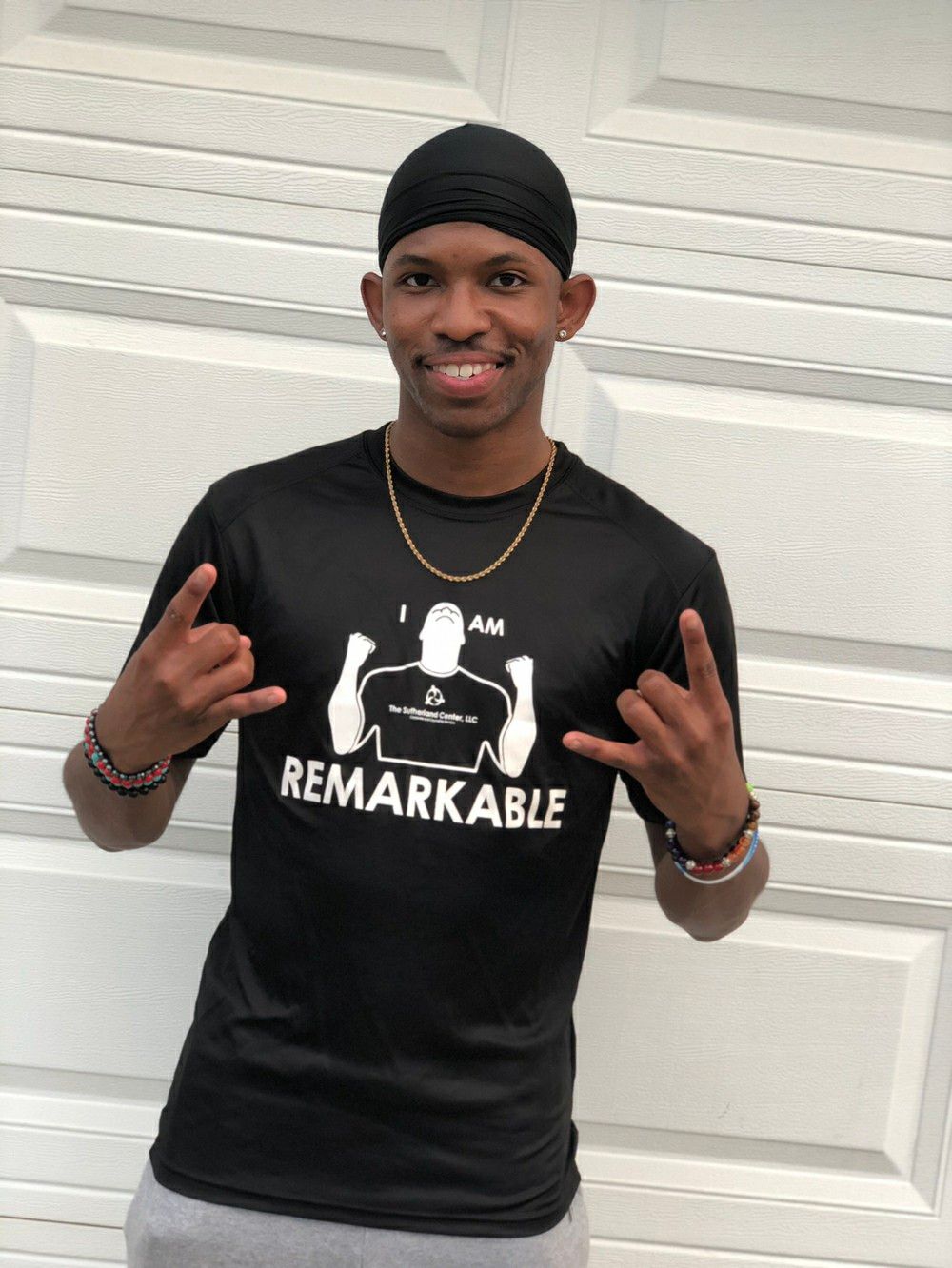 Smiling man in black “REMARKABLE” shirt and cap, posing in front of a white garage door.