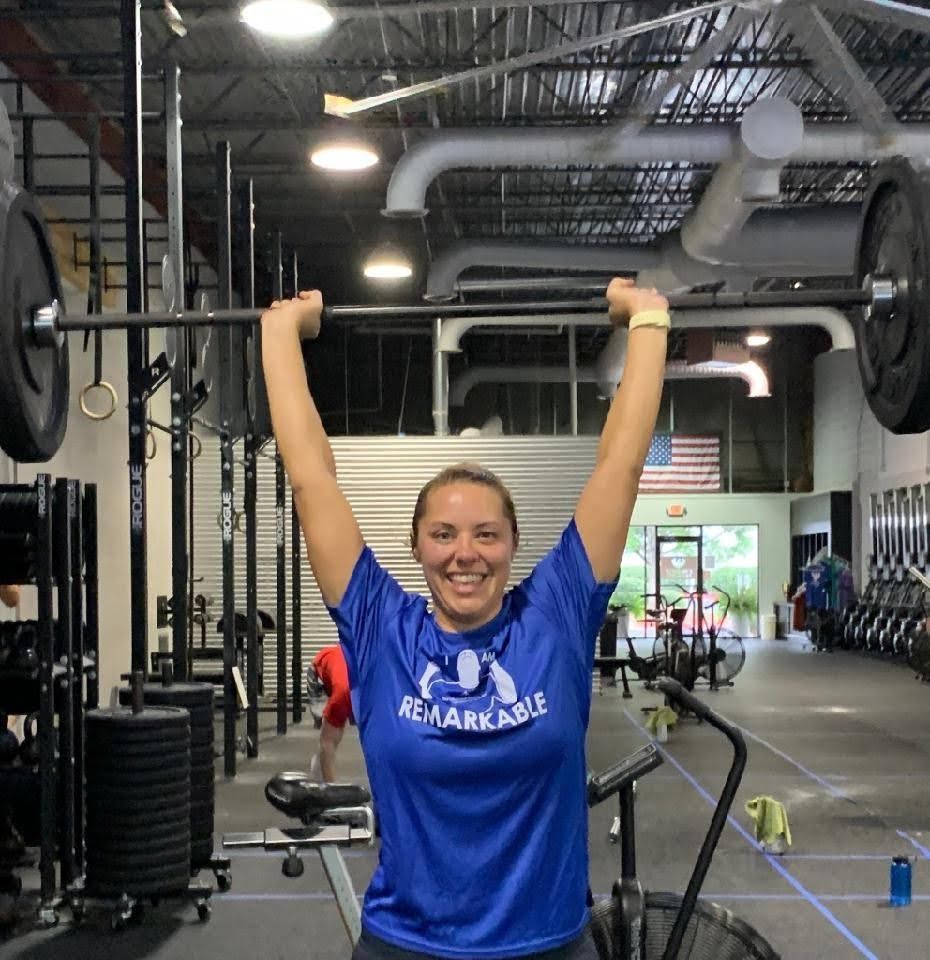 Woman in blue shirt lifting a barbell overhead in a gym