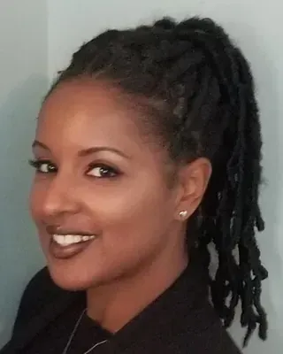 Portrait of a smiling person with dark dreadlocks, wearing a black top against a gray background