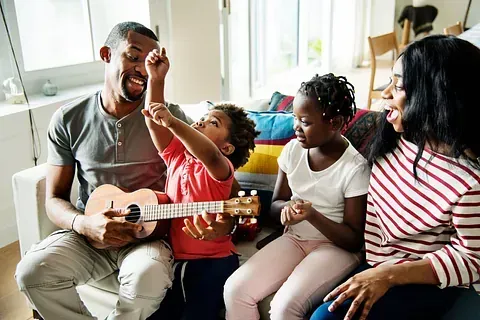 Family singing together on a couch, with a child holding a ukulele in a bright living room
