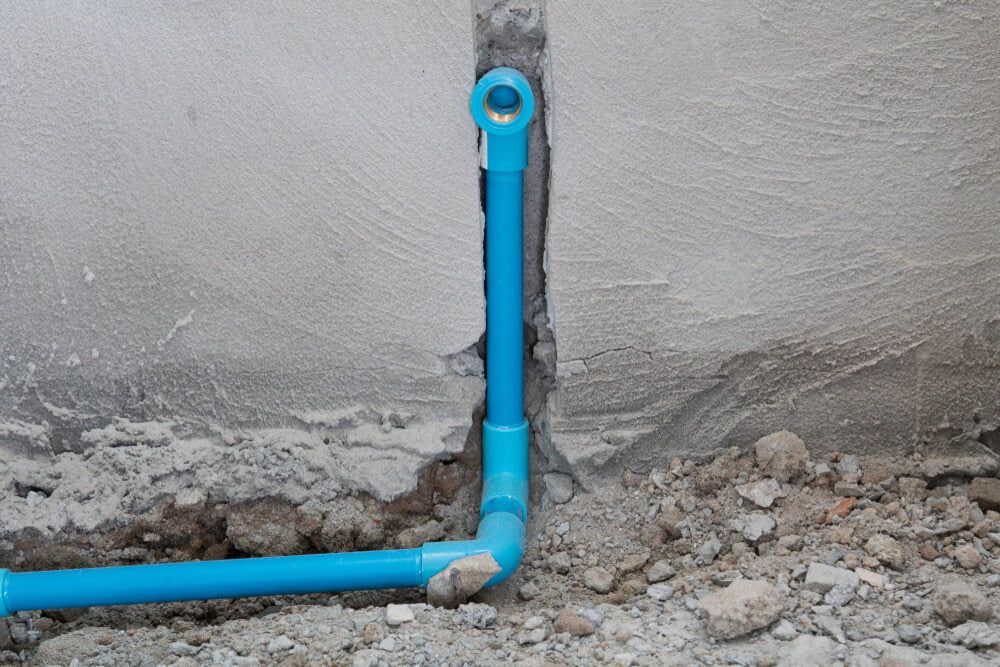 A Blue Pipe is Connected to a Wall in the Dirt — Daniel Gray Plumbing in Tumbulgum, NSW