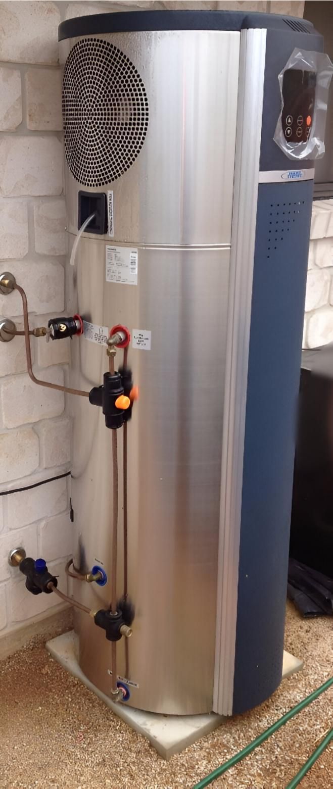 A Stainless Steel Water Heater is Sitting on the Floor Next to a Brick Wall — Daniel Gray Plumbing in South Murwillumbah, NSW