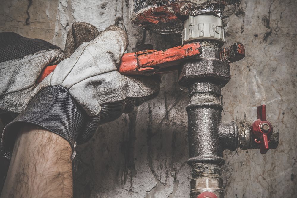 Gloved Hand Turning an Orange Valve on Rusty Plumbing Pipes — Daniel Gray Plumbing in Chillingham, NSW