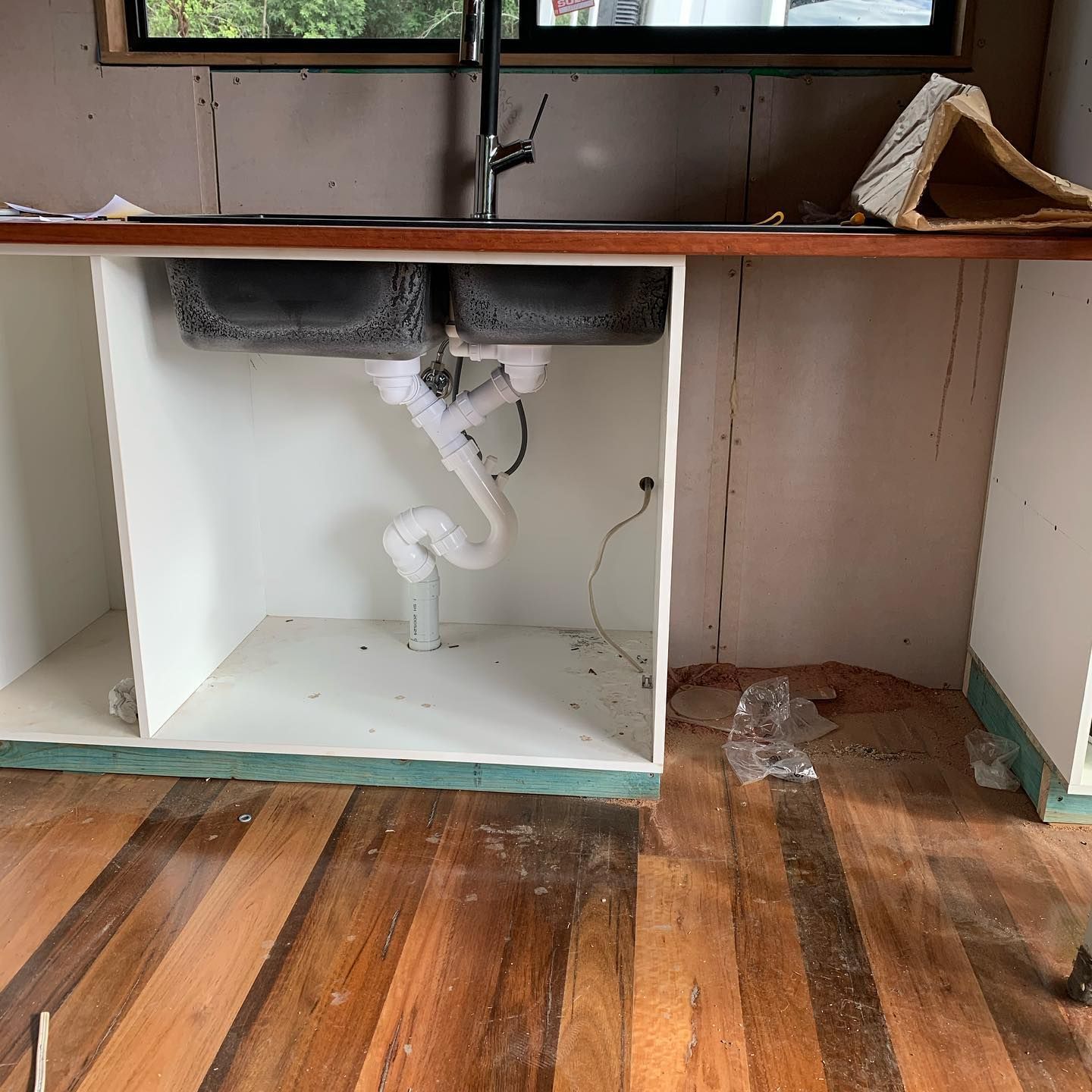 Kitchen under-sink with double basins, plumbing, and exposed cabinets and walls under construction. — Daniel Gray Plumbing in Tyalgum, NSW