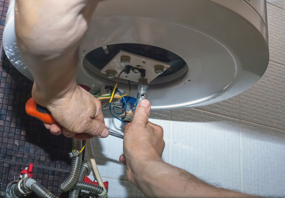Hands Using Tools to Work on a Water Heater Inside a Utility Area — Daniel Gray Plumbing in Uki, NSW