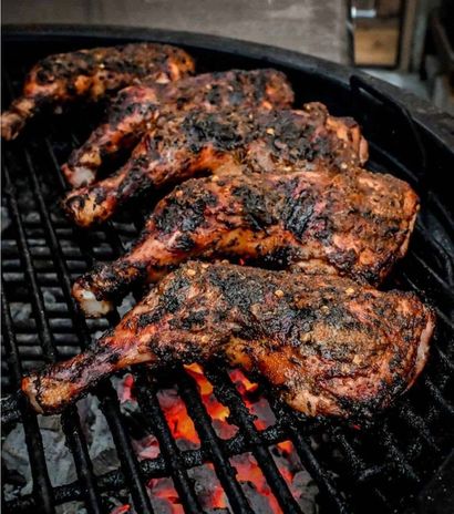 Grilled barbecue chicken pieces sizzling over charcoal, charred and smoky on a black grill.
