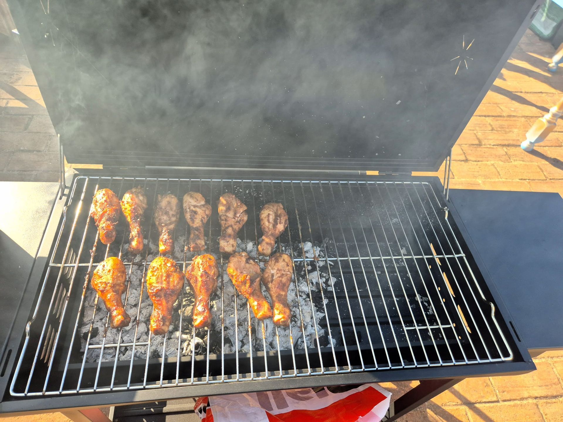 Chicken wings grilling on a barbecue, with smoke rising and one browned rack on a charcoal grill