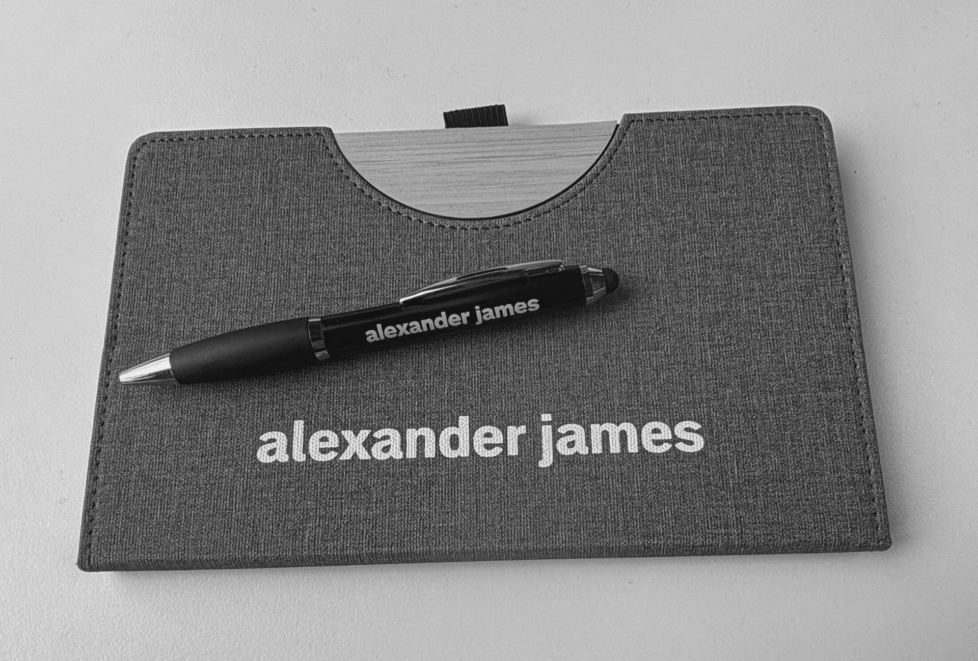 Gray Alexander James note book with a black pen with Alexander James on it, on top