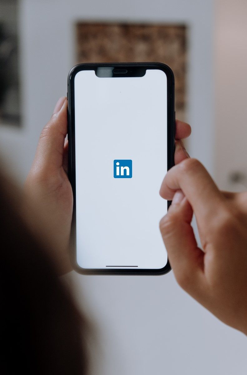 Hands holding a smartphone displaying the LinkedIn app logo on a white screen.