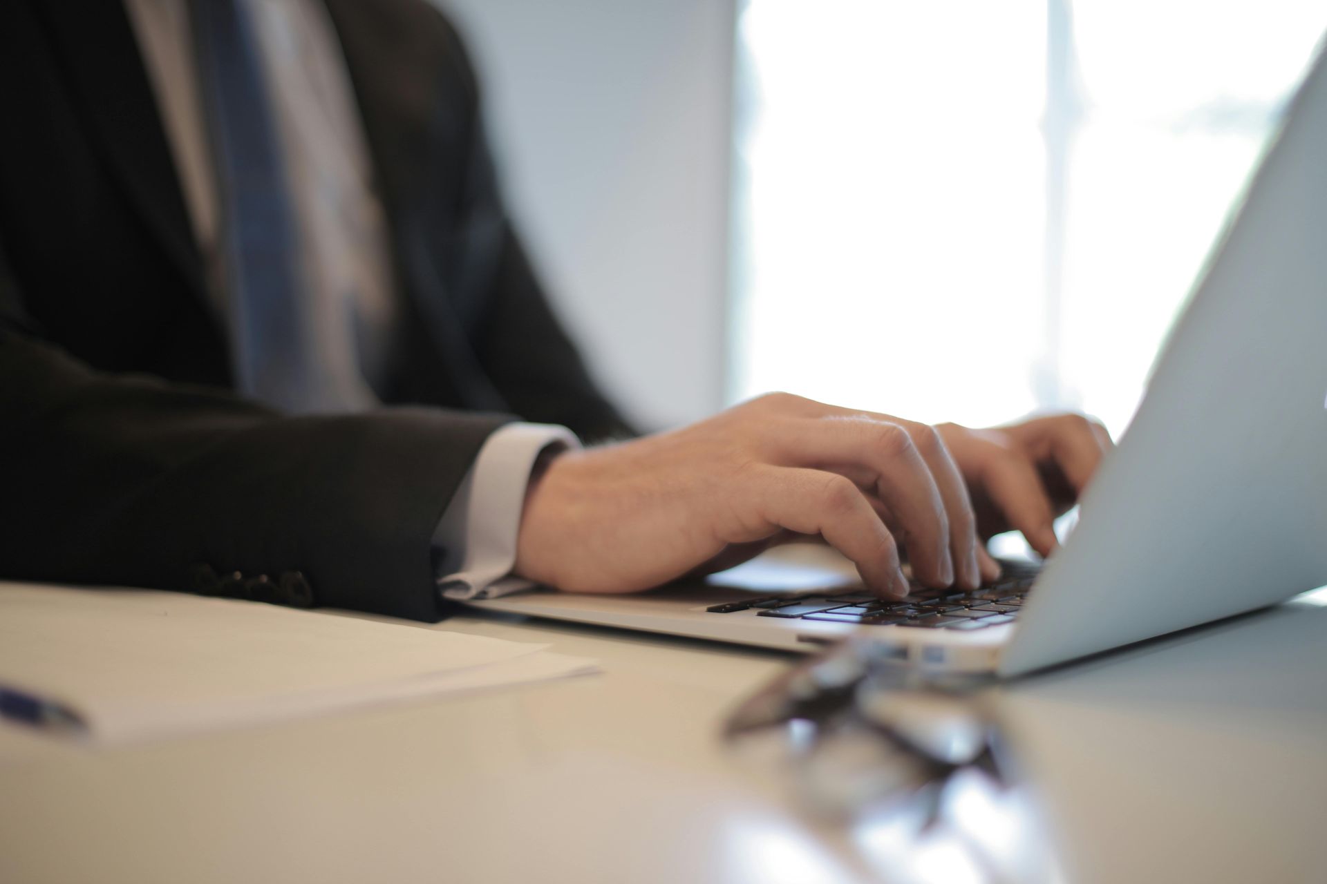 Close-up of businessman typing on a laptop in a modern office setting, showcasing remote work