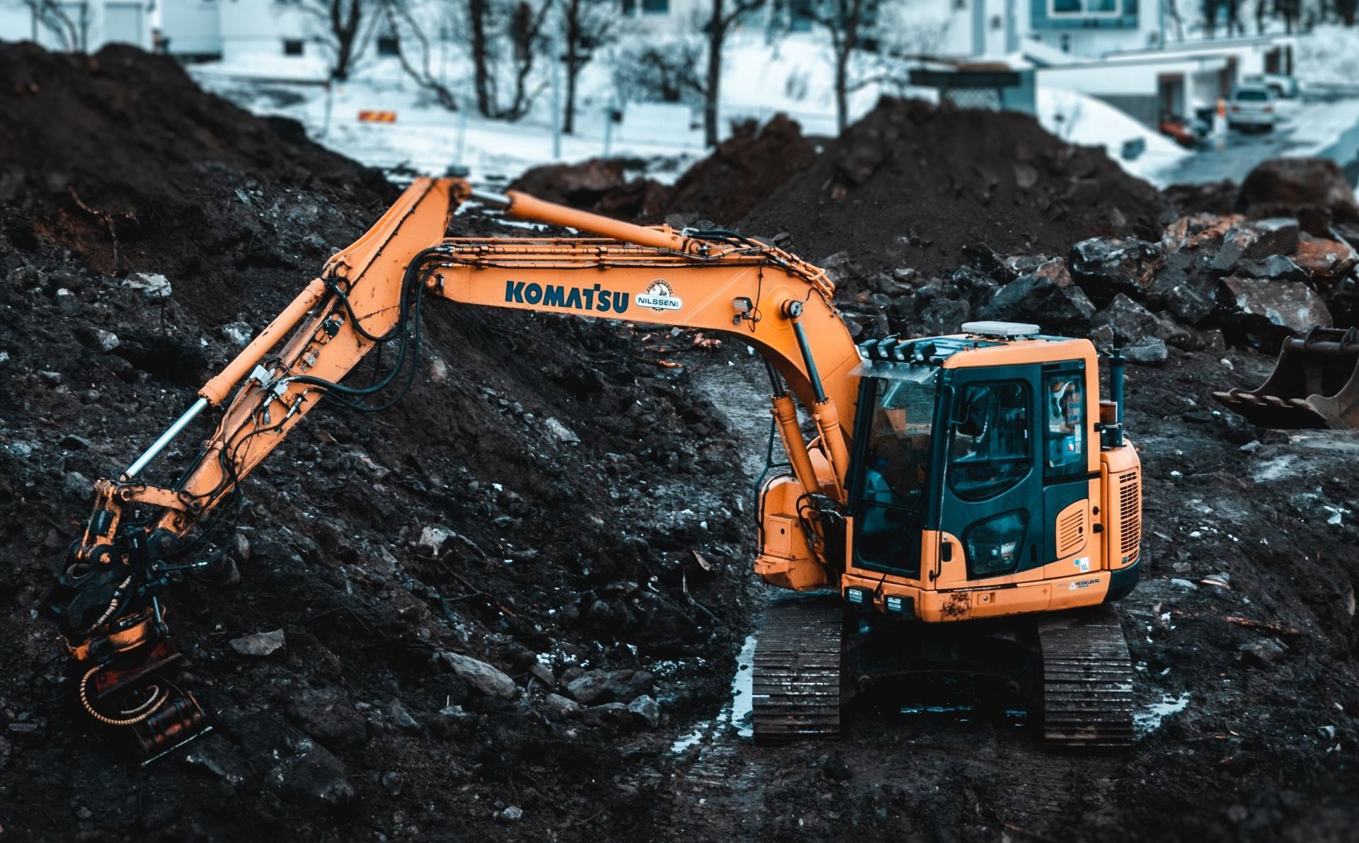 Yellow Komatsu excavator on a construction site, digging into dark soil. 