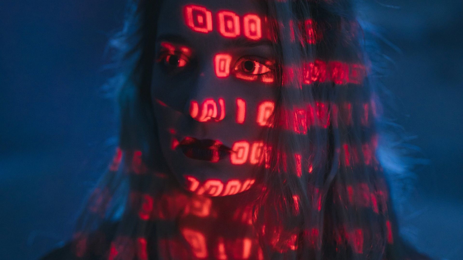 A woman's face is partially obscured by a red binary code projection.