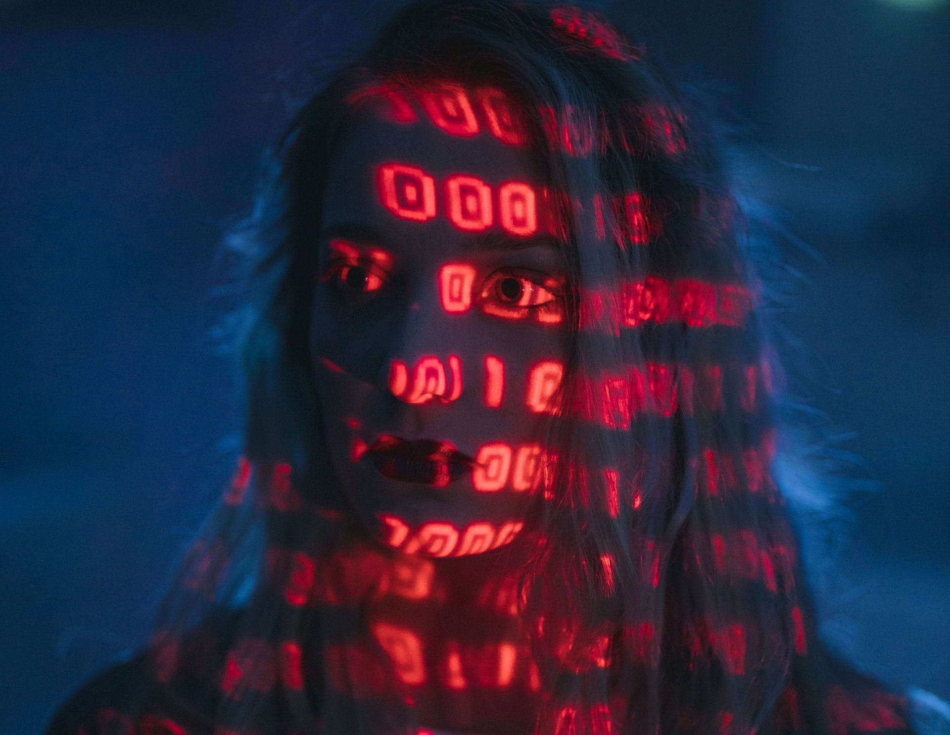 Woman with red binary code projected onto her face, blue background.