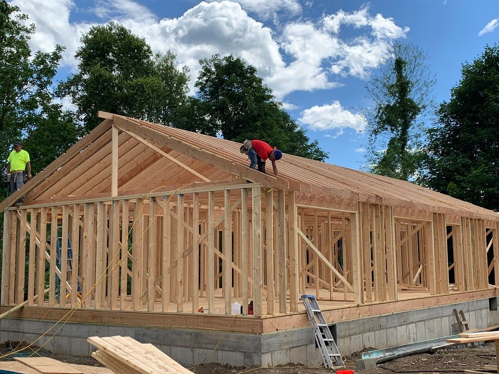 Workers framing a house with wood on a concrete foundation under a blue sky