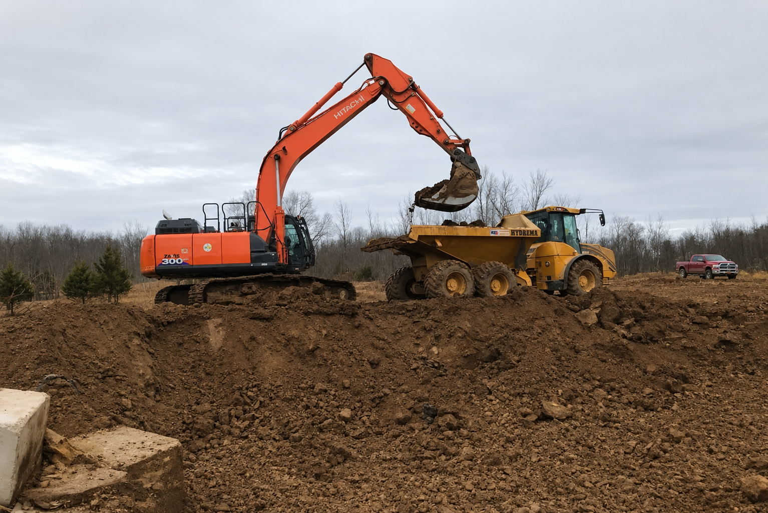 Excavator loading dirt into a yellow dump truck at a muddy construction site