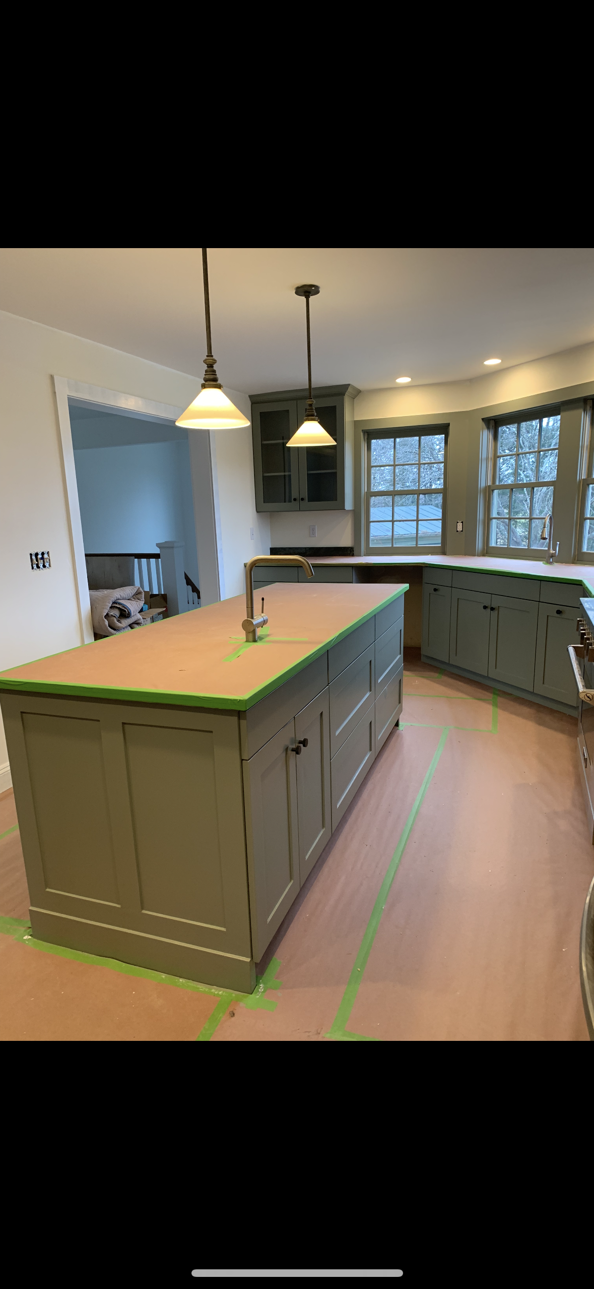 Modern kitchen with green island, pendant lights, wood floors, and windows