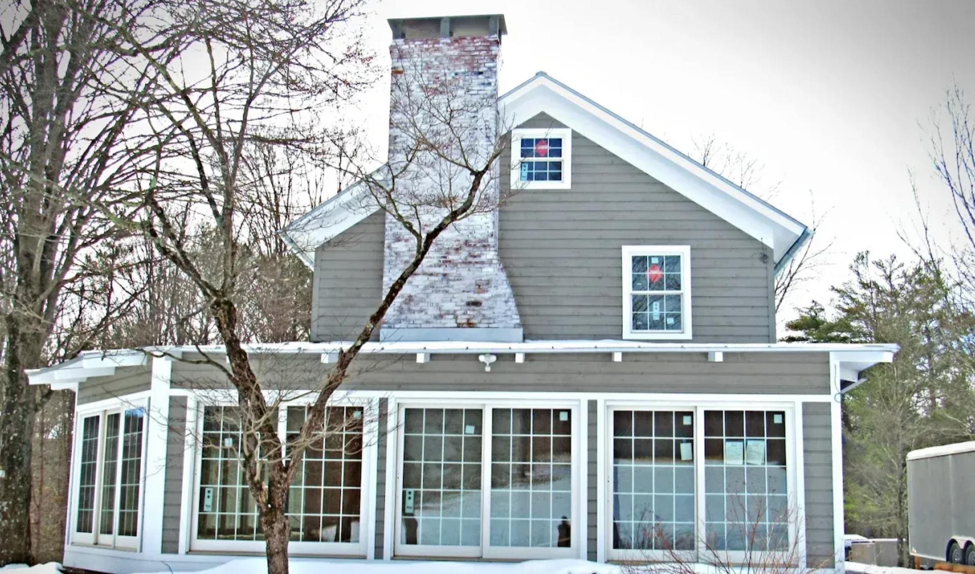 Snow-covered gray house with a stone chimney and screened porch in winter