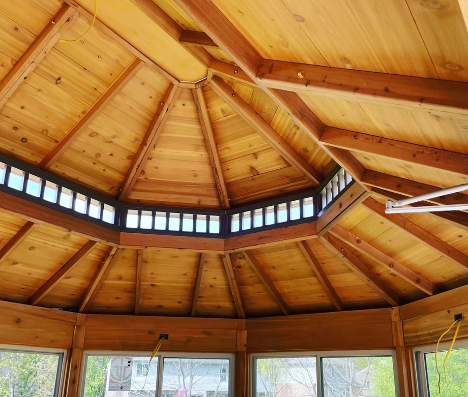 Wooden gazebo ceiling with radial beams and a ring of windows above glass doors