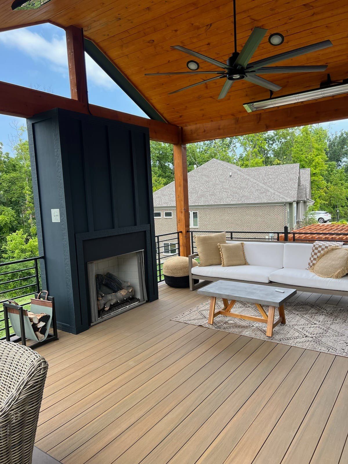 Covered outdoor patio with wood ceiling, ceiling fan, fireplace, and beige seating around a coffee table.