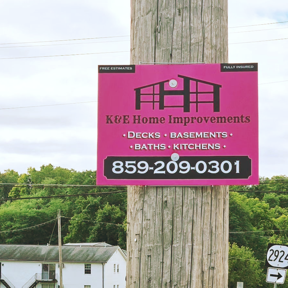 Pink K&E Home Improvements sign on a wooden utility pole with phone number 859-209-0301.
