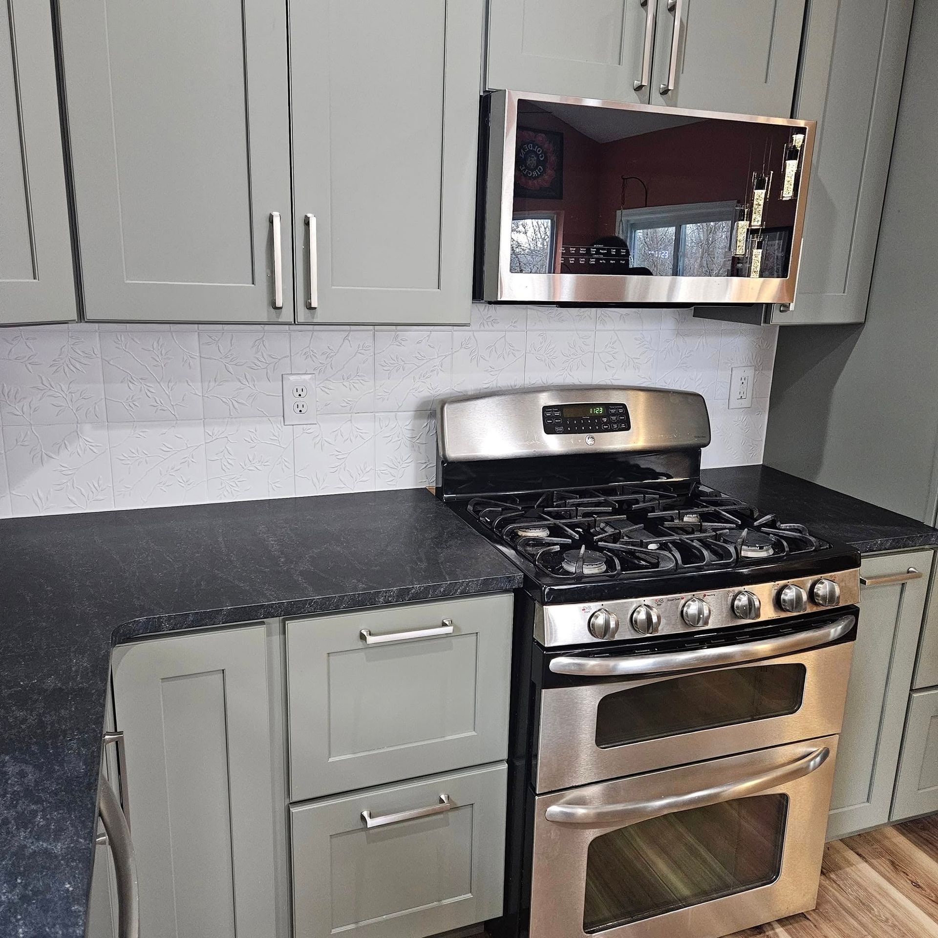 Modern kitchen with gray cabinets, black countertops, stainless steel stove, and built-in microwave.