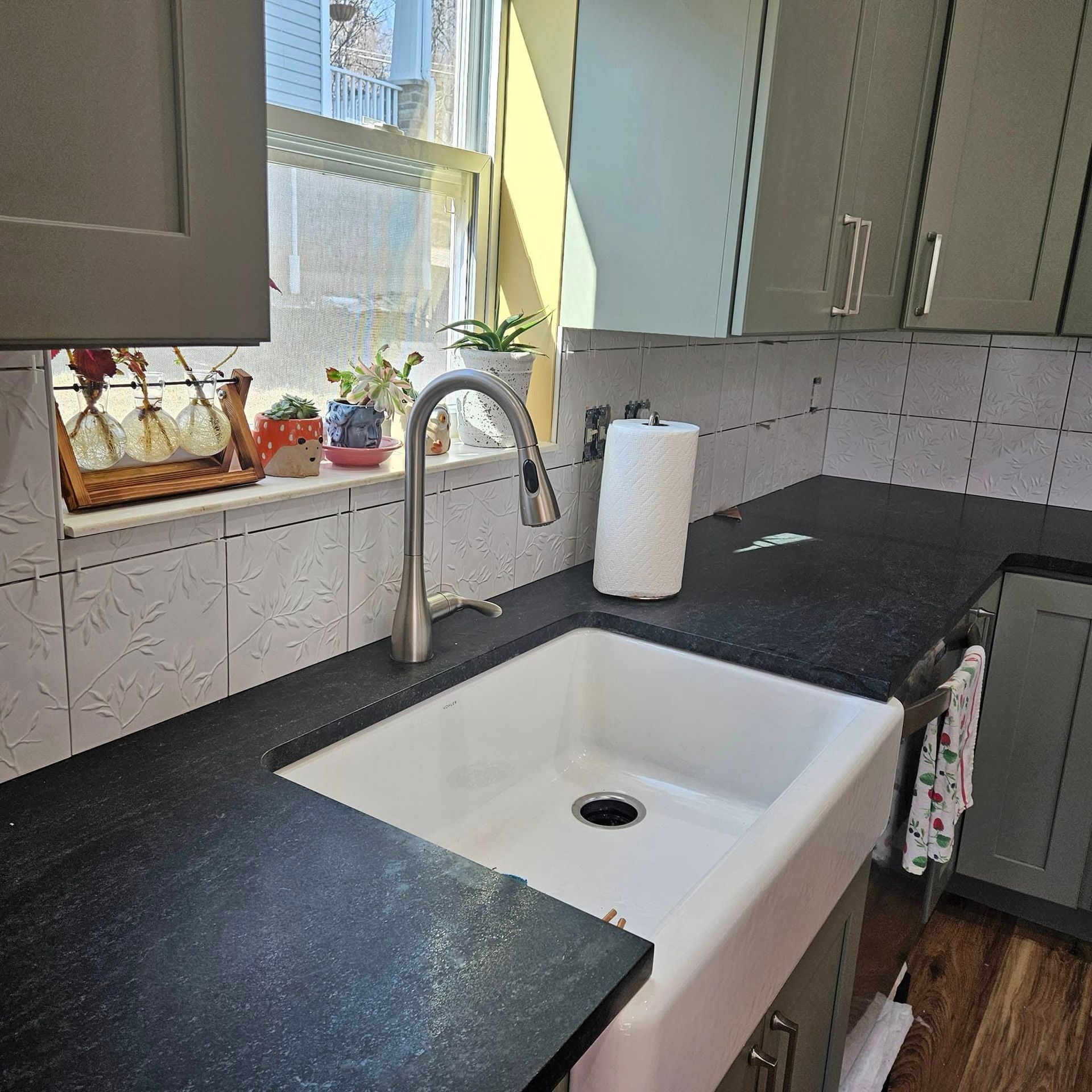 Kitchen sink with black countertop, window, paper towel roll, and potted plants.