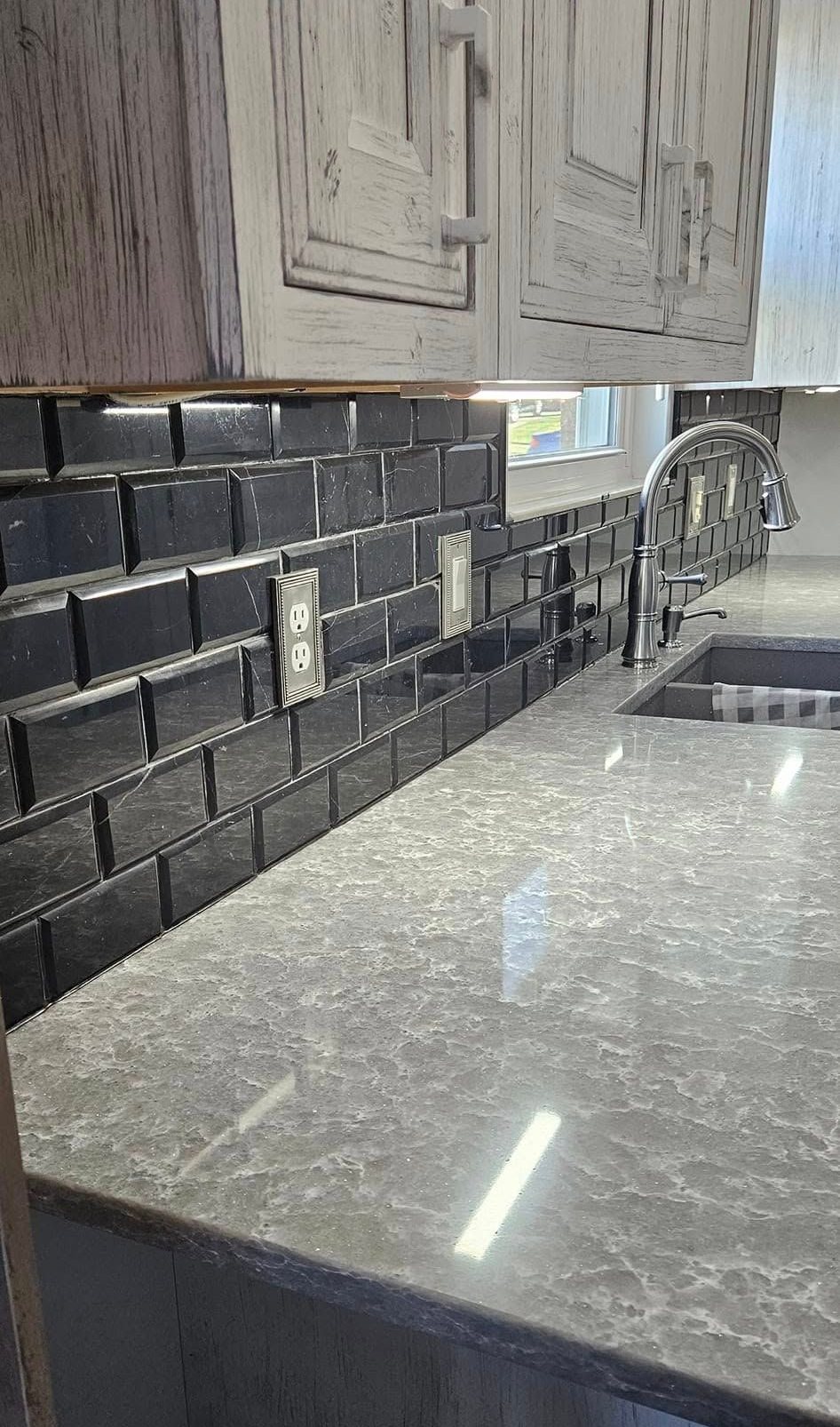 Kitchen with dark subway tile backsplash, gray countertop, and light wood cabinets above.