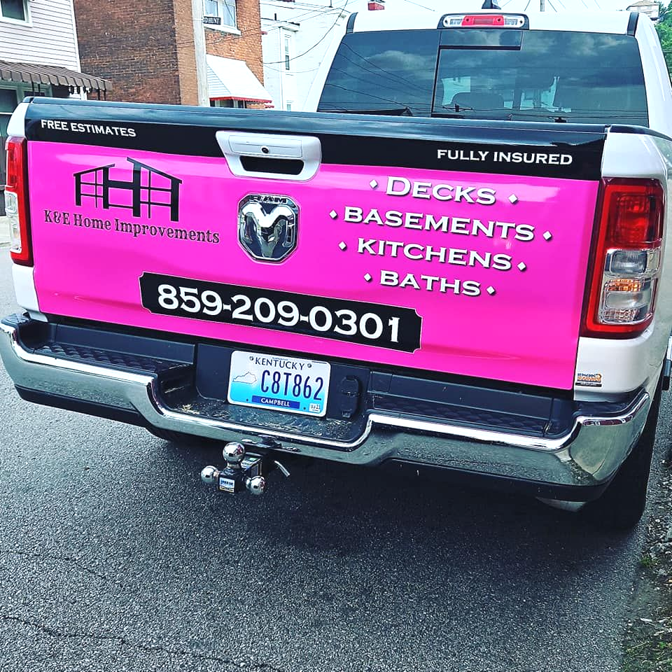 Pickup truck with bright pink contractor banner advertising decks, basements, kitchens, and baths.
