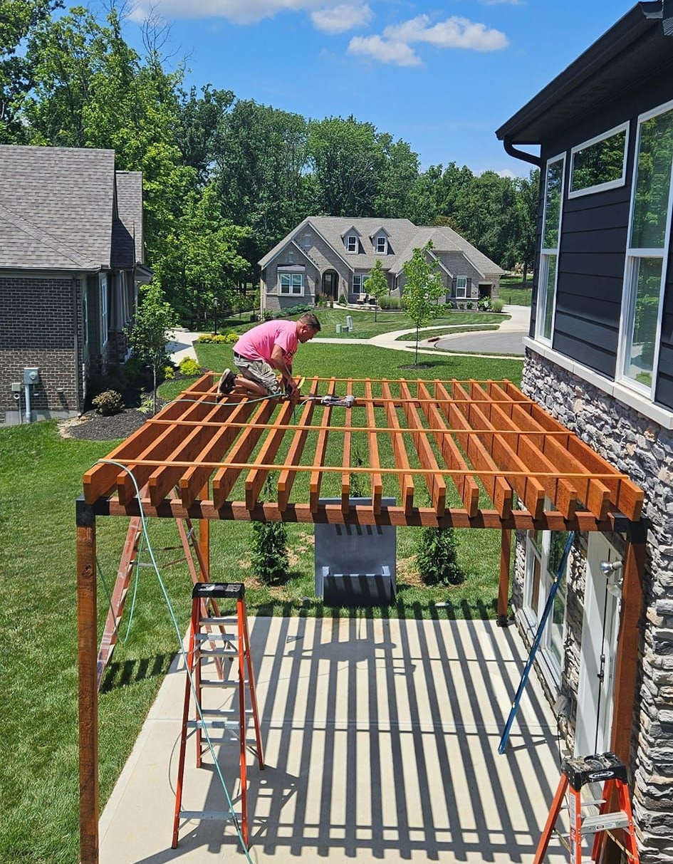 Person building a wooden pergola frame in a suburban backyard, with ladder and house in view
