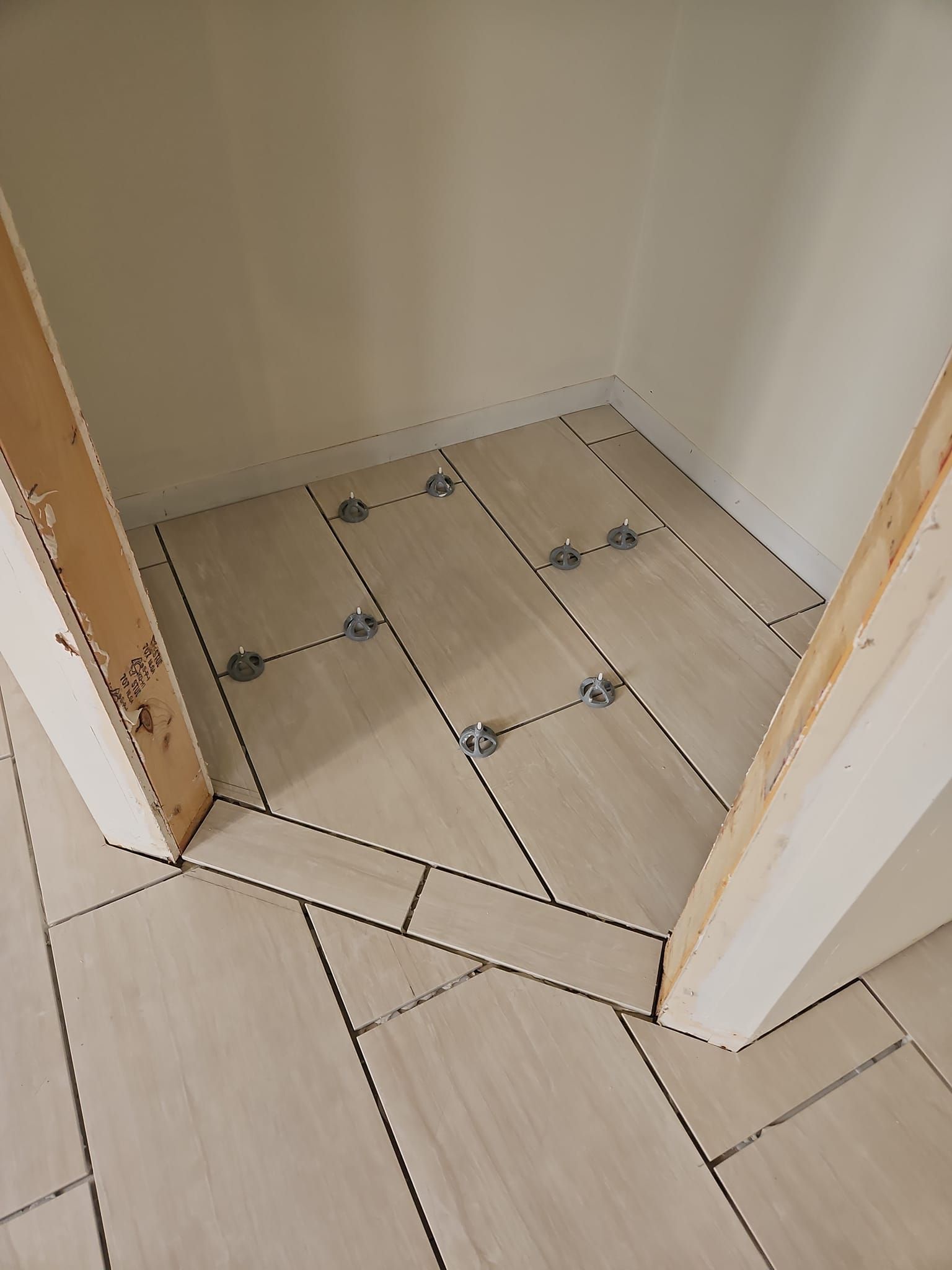 Tiled floor area in a doorway, with several tiles lifted and exposed adhesive marks.