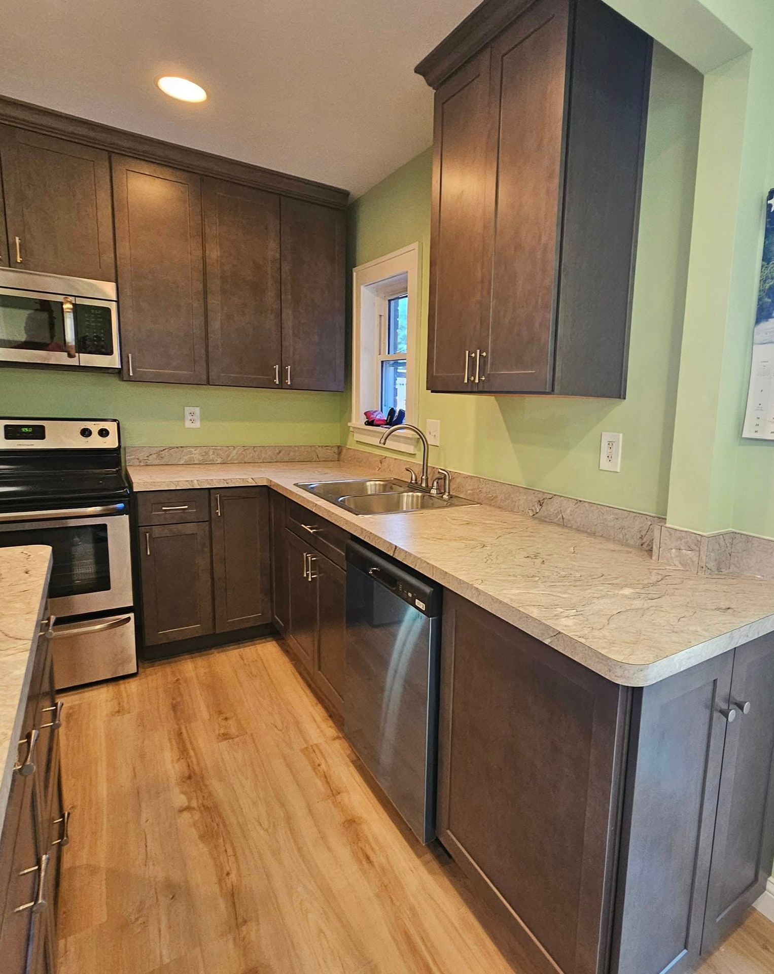 Modern kitchen with dark wood cabinets, light countertops, stainless appliances, and pale green walls
