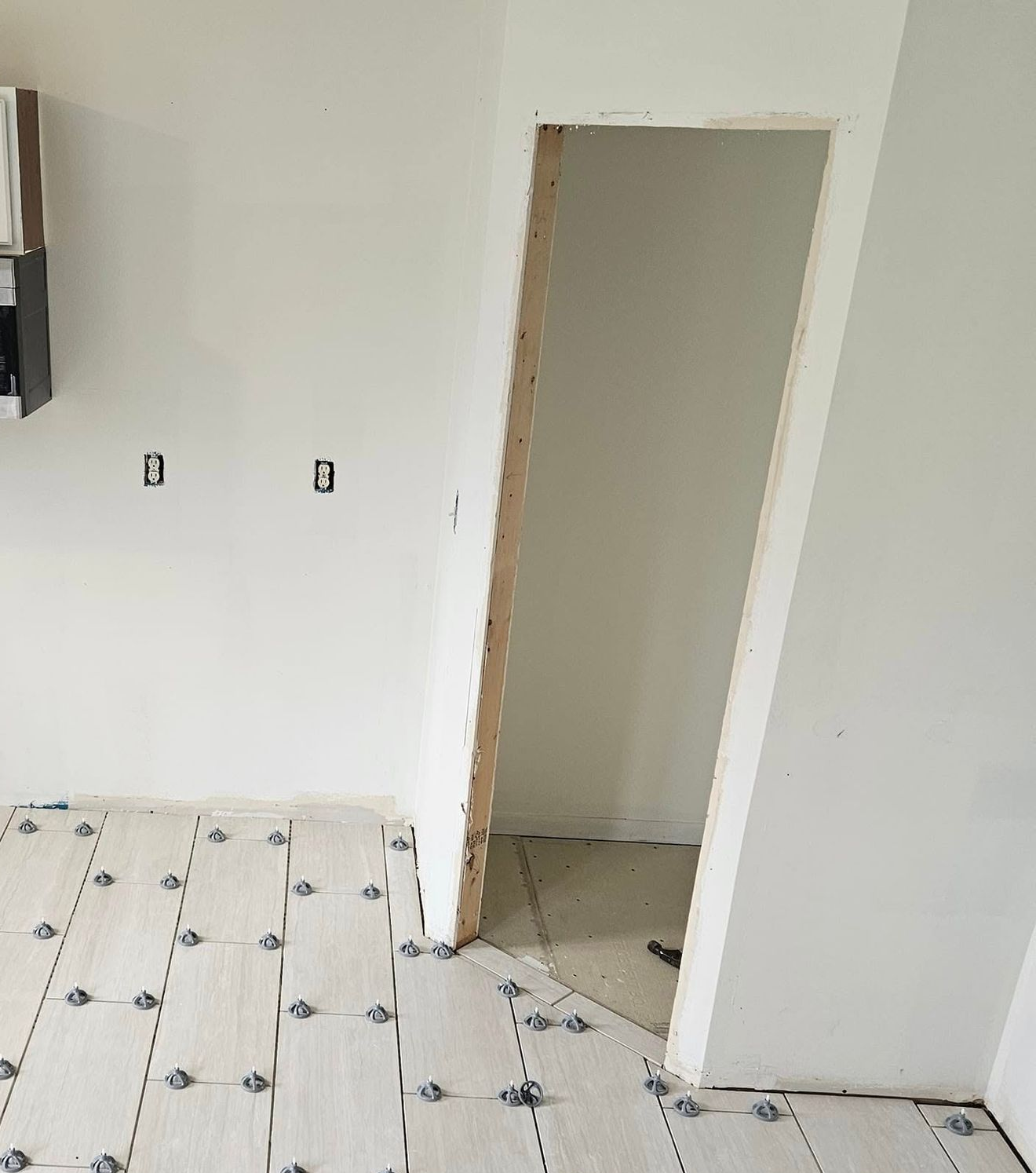 Empty unfinished room with white walls, tiled floor, and a doorway opening into another room