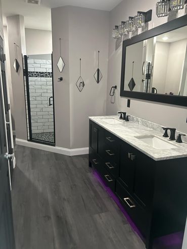 Modern bathroom with gray walls, dark vanity, large mirror, and tiled shower area.